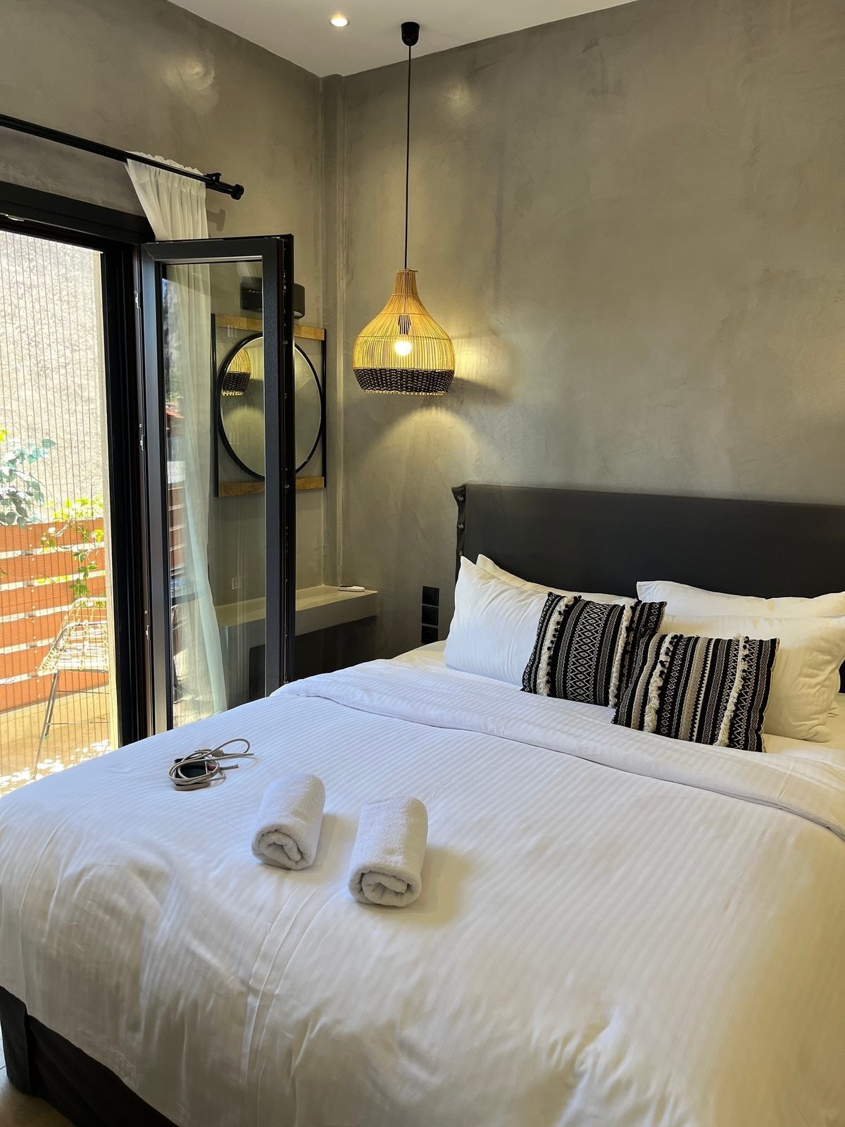 Oikia Guesthouse 臥房，灰牆藤編吊燈與黑色鐵件床架